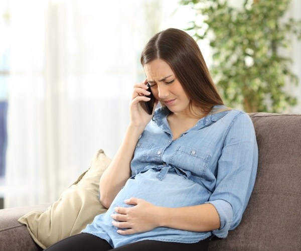 pregnant woman on couch on phone looking anxious