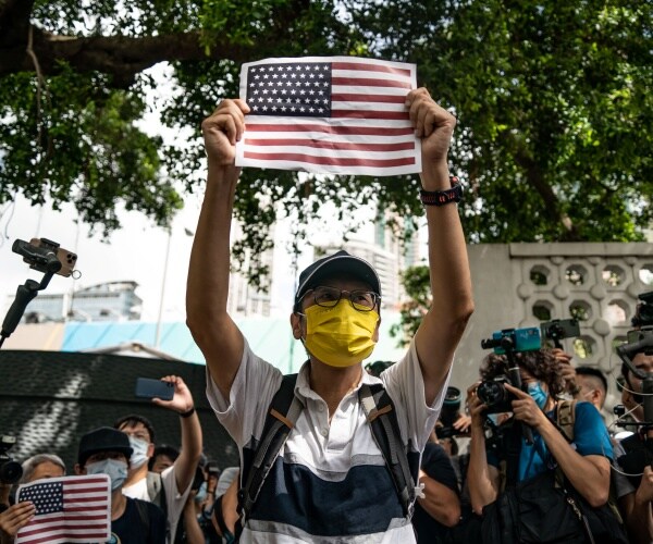 man wearing yellow face mask holds up a cut out of the american flag