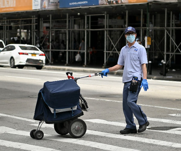 a postal worker is shown wearing his uniform, face mask and gloves