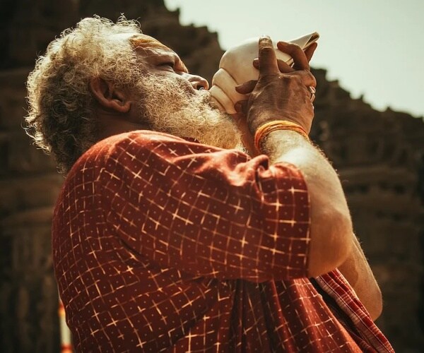 man blowing into a conch shell