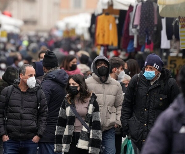 People, some wearing surgical masks, others FFP2 masks, stroll past stalls at the Porta Portese open air market