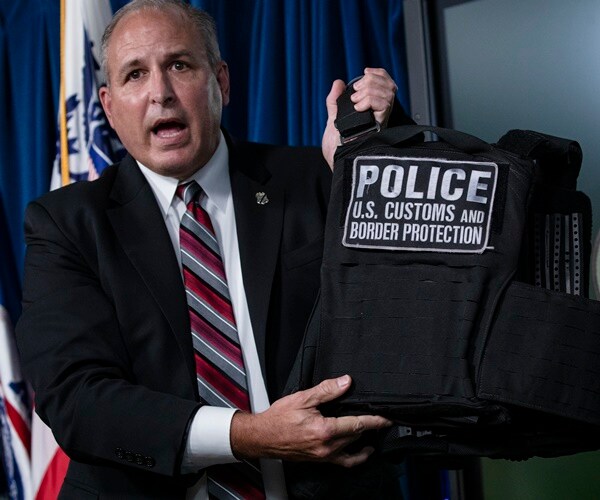 mark morgan holds  up a vest that says police u.s. customs and border protection
