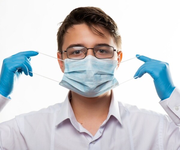 person in glasses and blue surgical gloves putting on mask