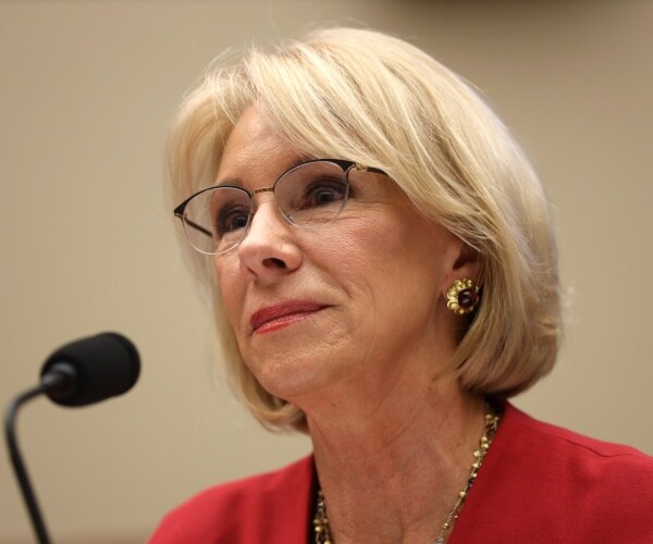 betsy devos in a bright red blazer speaking into a microphone