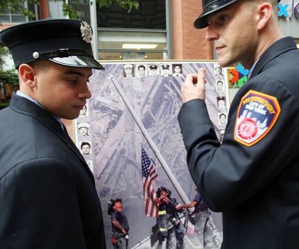 two firefighters with a photo of firefighters on nine eleven raising an american flag amid the rubble
