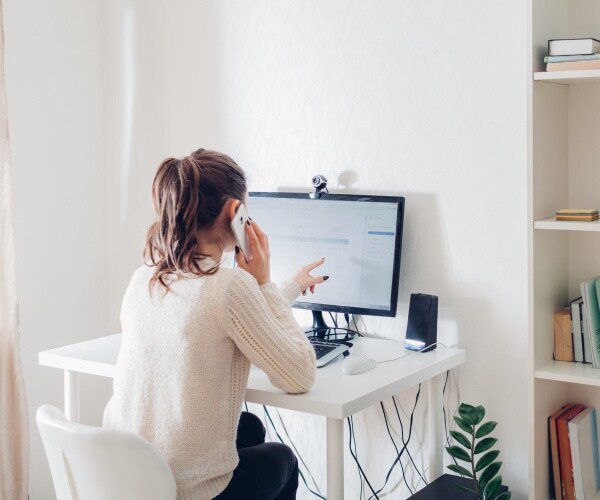 woman works from home at a desktop computer talking on the phone