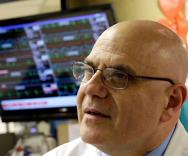 a doctor speaks to the media with digital medical information up on a screen behind him