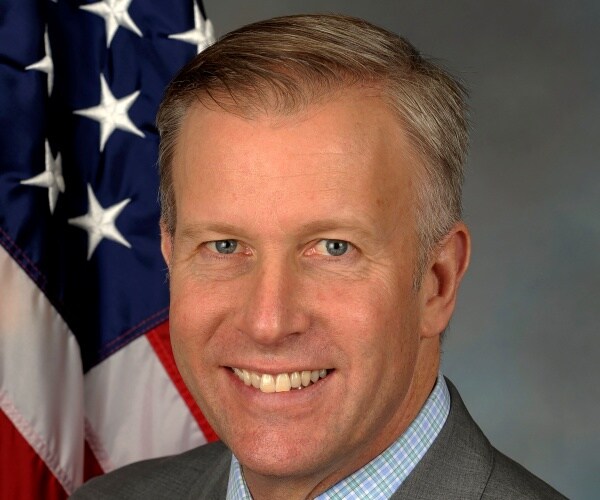jacobs in a gray suit and blue shirt in front of a us flag