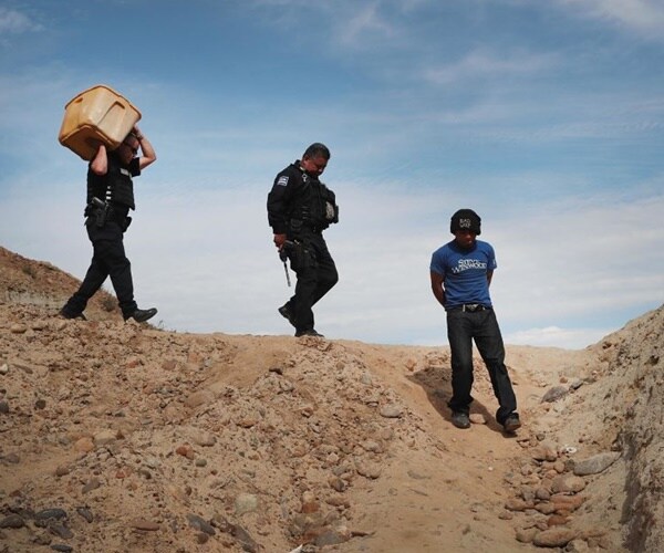 a guatamalan man is in handcuffs and walking with mexican police down a sanded area