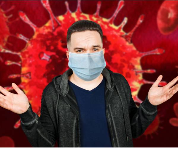 man in surgical mask throwing up hands in front of coronavirus image