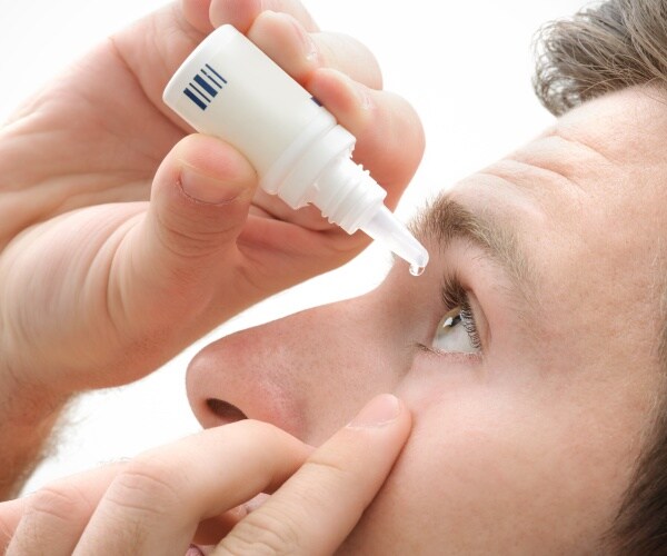 closeup of man putting drops in eye