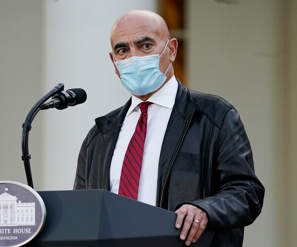 moncef slaoui stands behind podium wearing mask