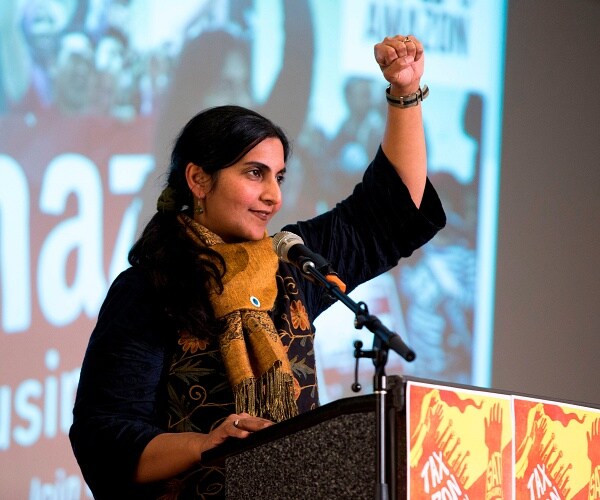kshama sawant stands behind podium with fist raised