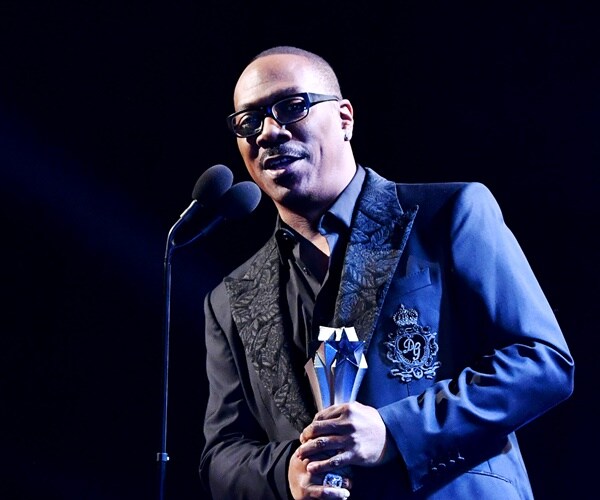 eddie murphy holds his award on stage under a blue light and speaks into the mic.