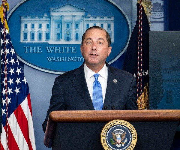 alex azar stands in front of flags at a white house podium
