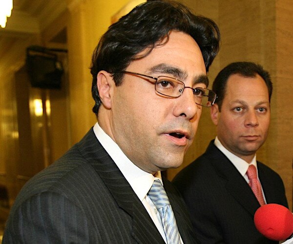 george sorial speaks into a mic during an interview with a british news station