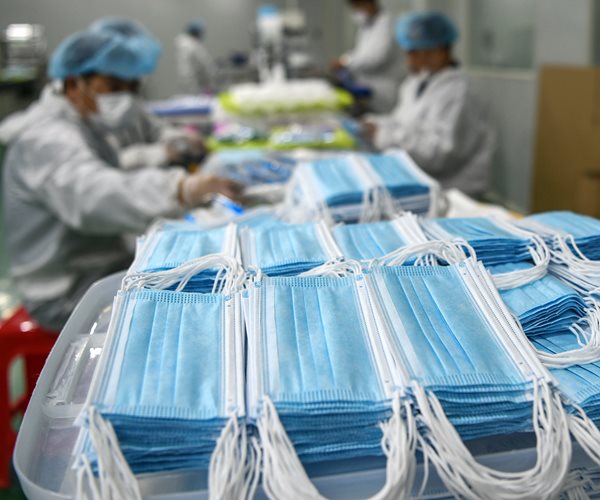 blue face masks piled up in front of workers at factory in china