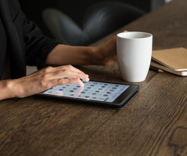 woman sitting at table with coffee surfing the web on tablet