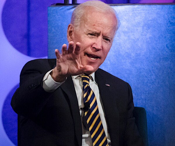 joe biden puts up his right hand while seated during a conference speech