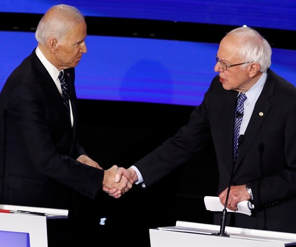joe biden and bernie sanders shake hands from behind podiums on a debate stage