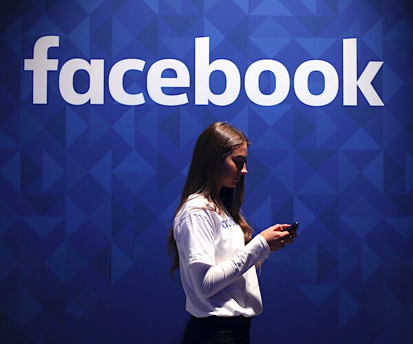 a girl on her smart phone walks past a facebook company sign at the offices