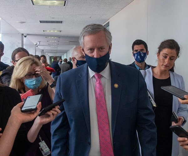 mark meadows walks with a clutch of people wearing a mask.