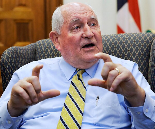 agriculture secretary sonny perdue sits and gestures with both hands while delivering his remarks