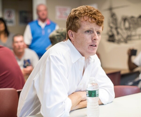 joe kennedy in a white dress shirt sitting at a table with a water bottle