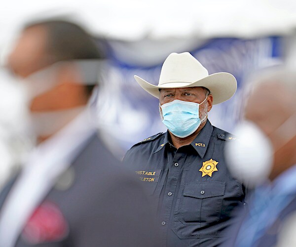 a police officer in the background wears a facemask