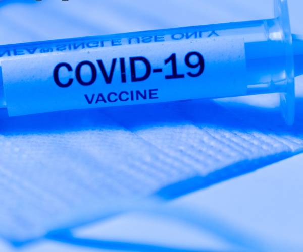 a syringe labled covid nineteen vaccine and a medical mask