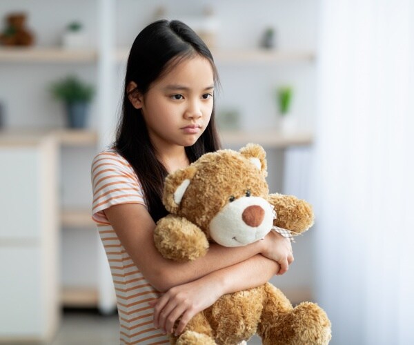 young girl looking sad and holding a teddy bear