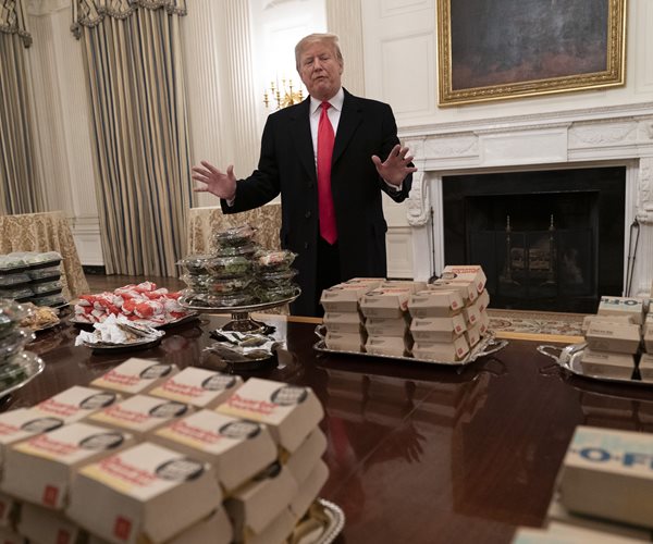 president donald trump stands at a table piled with fast food
