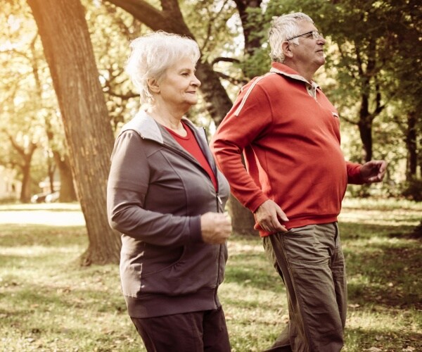 elderly couple jog outside with trees in the background