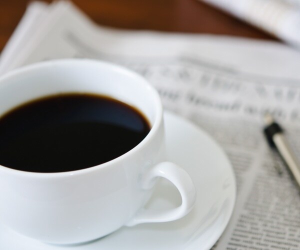 coffee in a white cup on top of a newspaper 