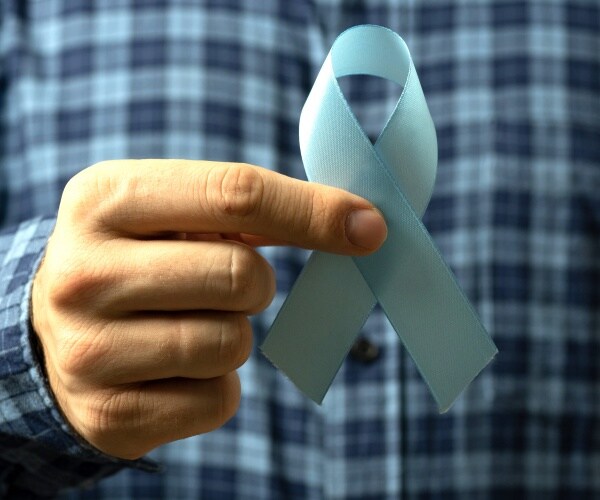 man in a plaid blue shirt holds a light blue ribbon for prostate cancer