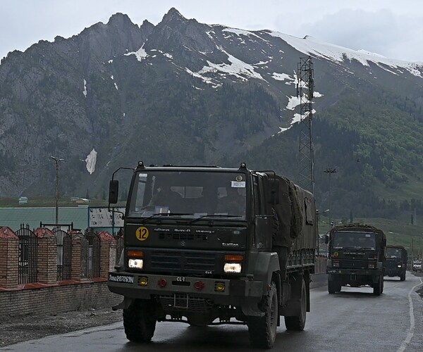 indian army trucks drive along a road in kashmir