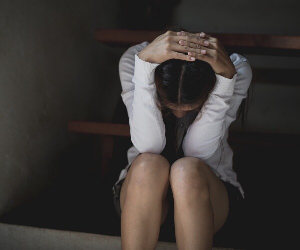 depressed young woman wearing a white top putting her hands on her head