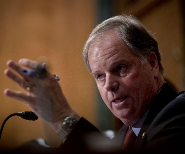 sen. doug jones gestures with his hands while holding a blue pen at a hearing on capitol hill