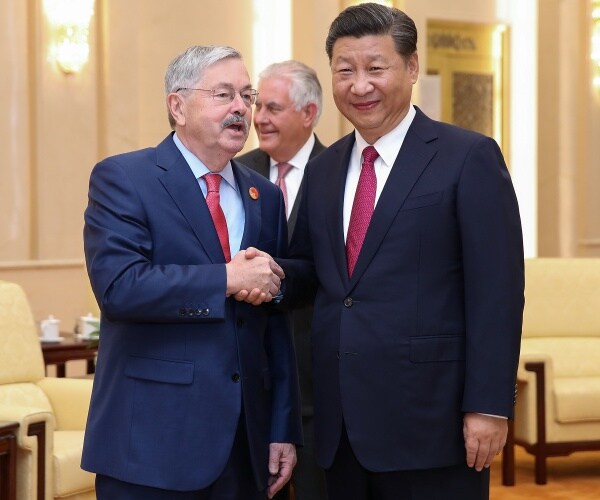 terry branstad in a navy blue suit shaking xi jinping's hand