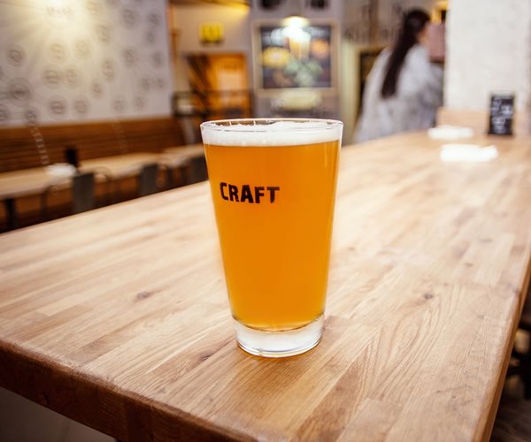 single pint glass of beer labeled craft on a long wooden table