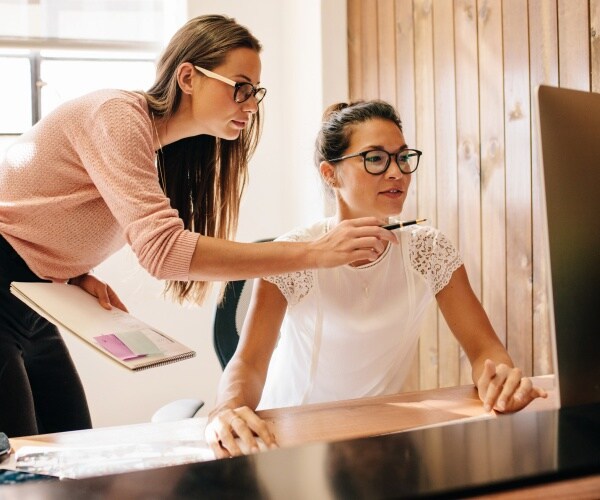 women working in an office with one sitting at a desk using a computer