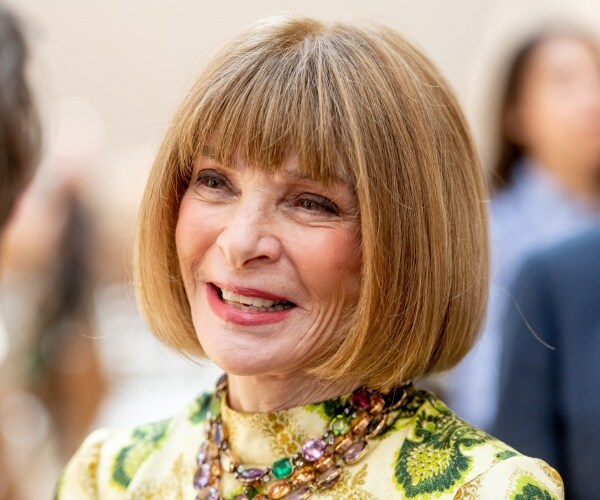 wintour in a green yellow and cream patterned dress and jeweled necklace smiling
