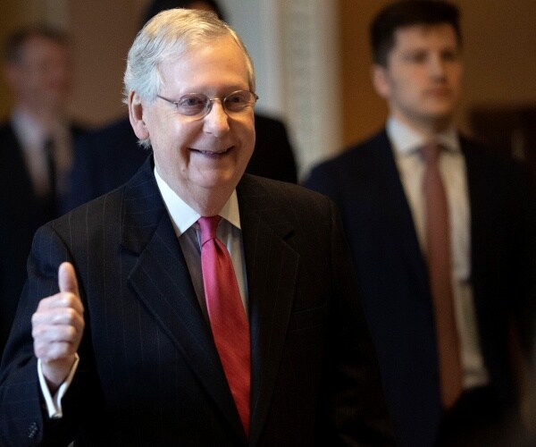 mcconnell smiling and giving a thumbs up wearing a suit and red tie