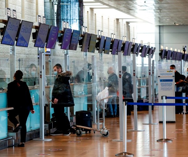 travelers wait by the check-in desk at the departures area of an airport