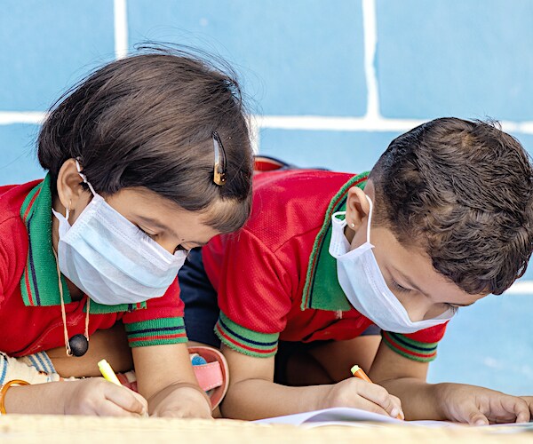 Kids busy in writing with medical face mask wearing due to covid-19 or coronavirus outbreak or pandemic at school