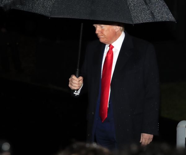 president donald trump stands underneath an umbrella as he walks out to head to a campaign rally