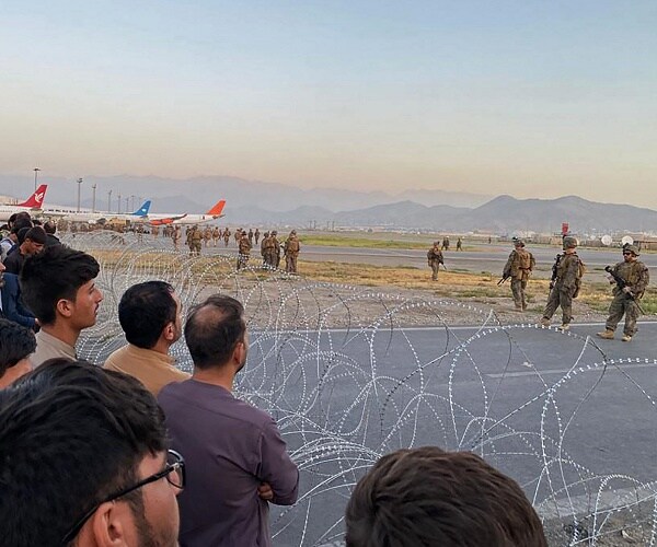 people crowd fence as soldiers guard airport