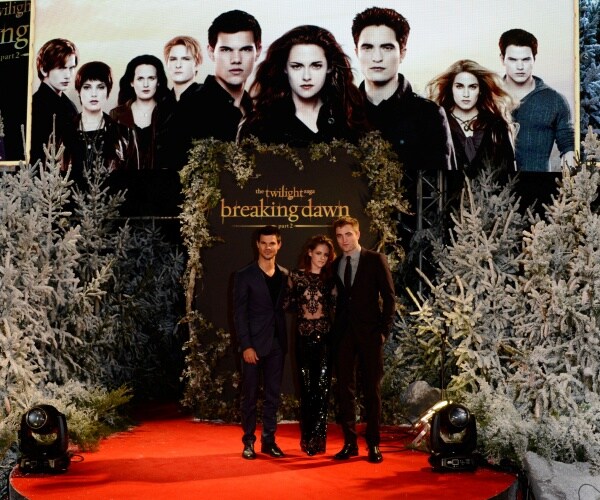 twilight movie poster with main characters in the background with three actors standing on a red stage