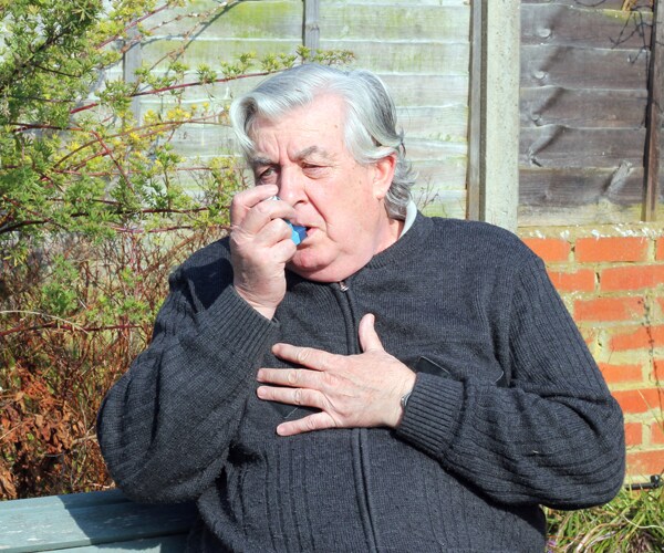 An elderly man using an inhaler