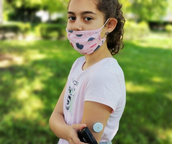 young girl wearing mask, checking her glucose levels with monitor